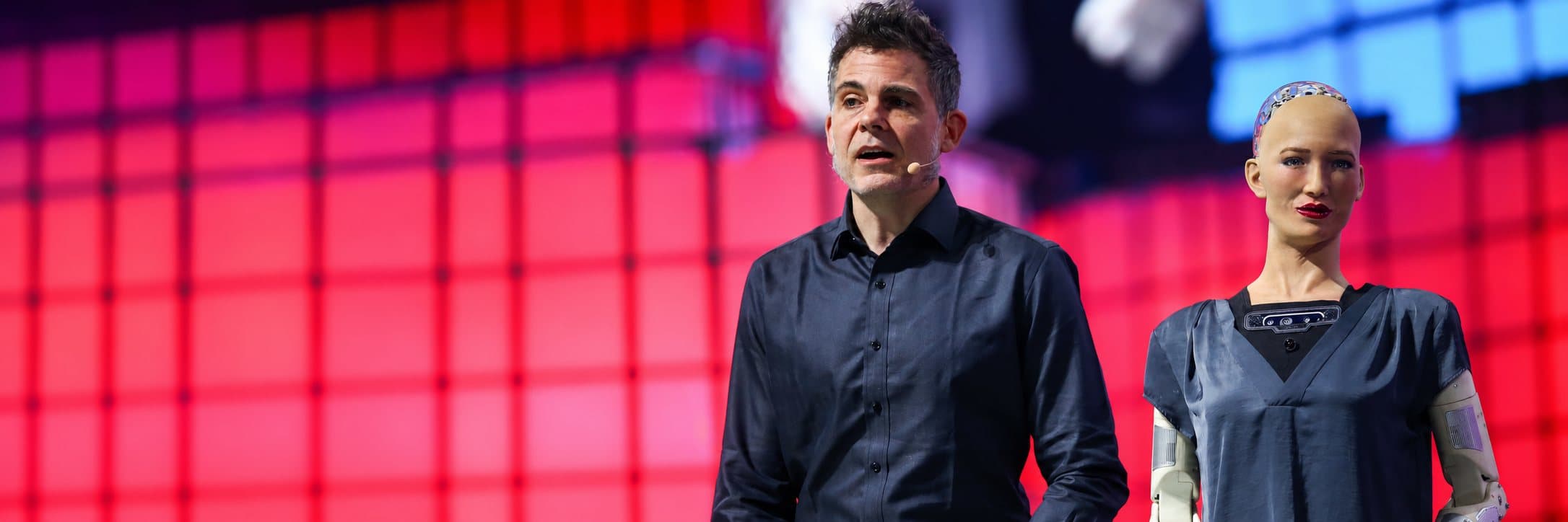 Spreker op het podium van Web Summit naast een humanoïde robot