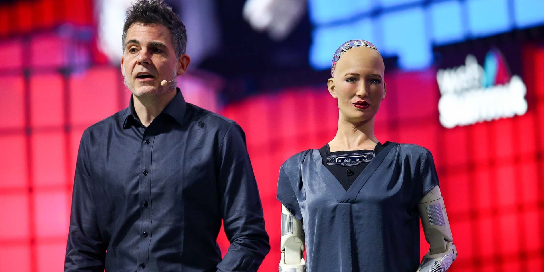 Spreker op het podium van Web Summit naast een humanoïde robot